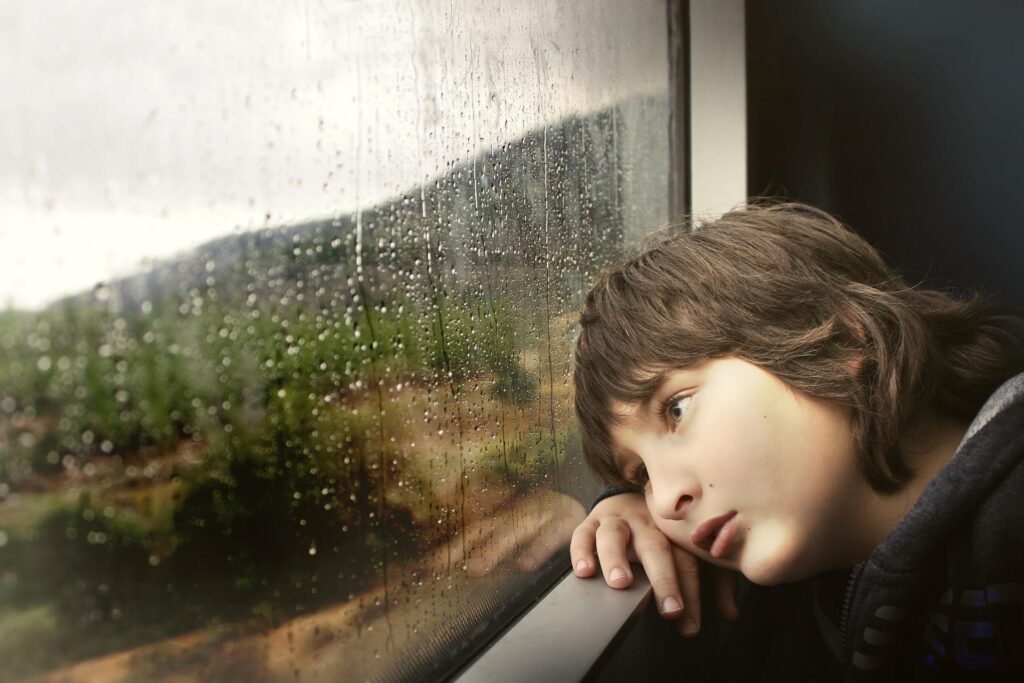 A sad boy staring out a window.